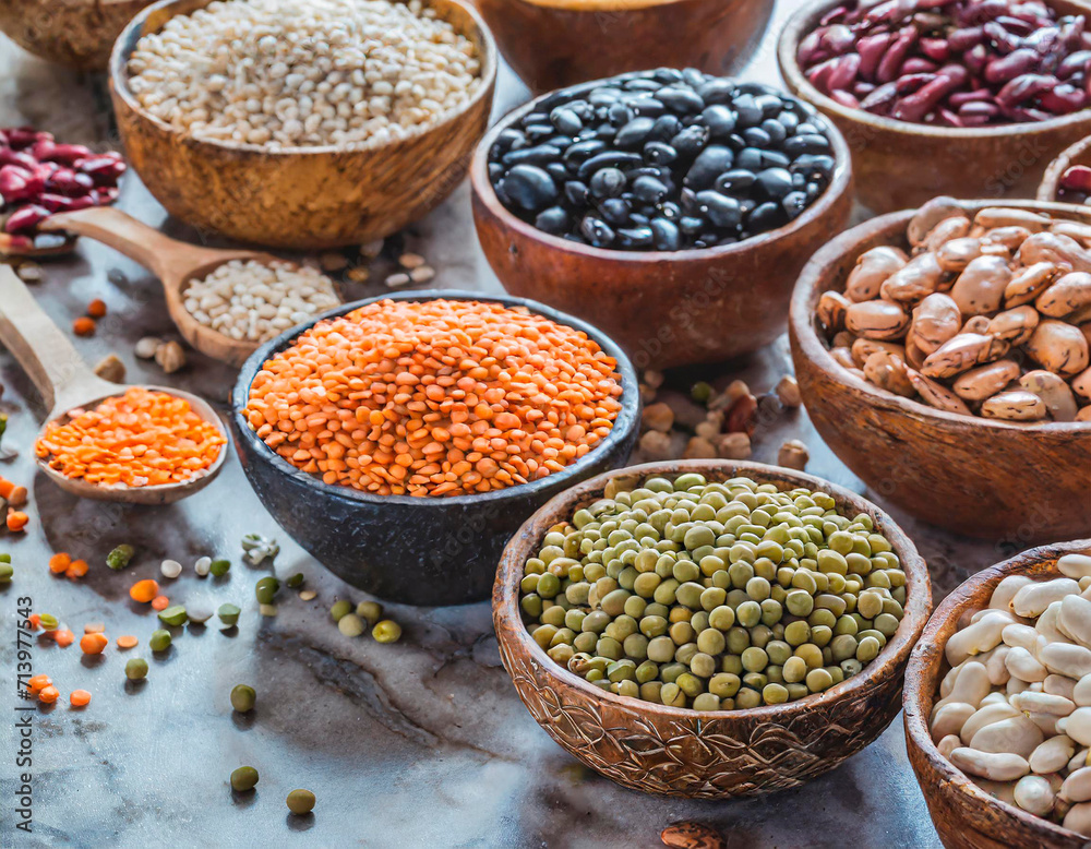 Top view of various bowls of legumes of various types and colors on a dark wooden kitchen table. Healthy food concept and detox or vegan menu. World Pulses Day.