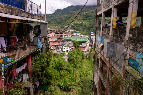Banaue, Ifugao, Philippines - View of a rural town nestled in green hills as seen between 2 buildings.