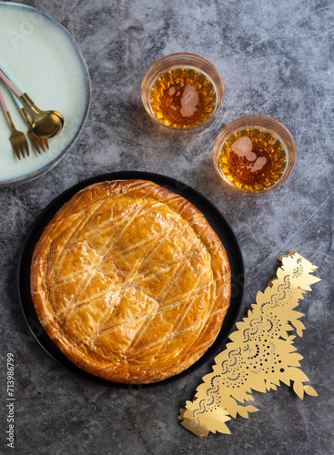Top view of traditional French galette des rois cake on a table with crown  with plate and glasses of cider. Tradition cake usually served on Epiphany, made with puff pastry and creamy almond filling