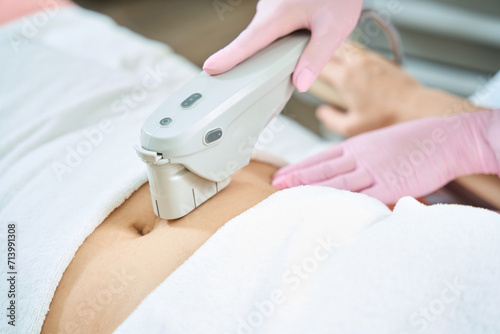 Cropped image of female beautician doing laser depilation of woman belly