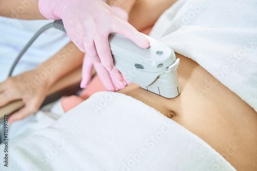 Beautician doing laser depilation of woman belly in blurred beauty salon