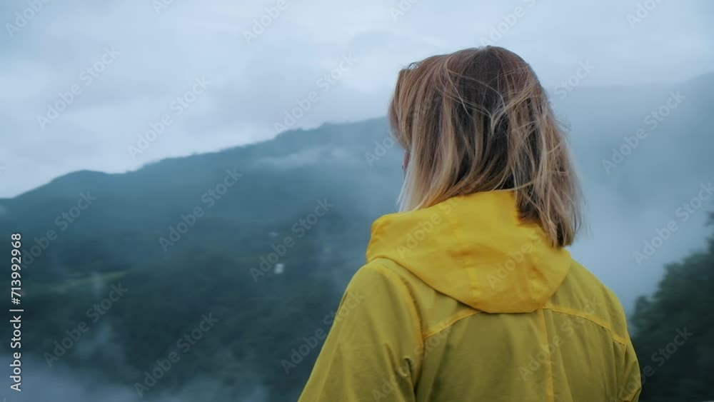 Female traveler in yellow raincoat looking from bridge in foggy mountains Female traveler in yellow raincoat looking from bridge in foggy mountains