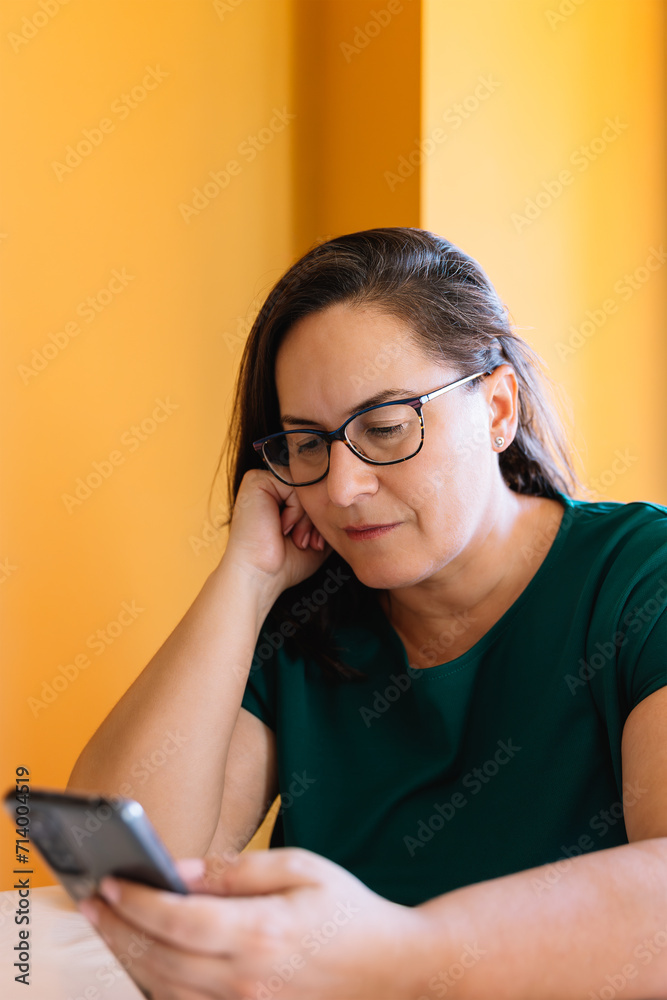 Portrait of 50 years old woman with loose brown hair and glasses, looking at her cell phone with relaxed and calm attitude. Concept of technology and mature age Portrait of 50 years old woman with loose brown hair and glasses, looking at her cell phone with relaxed and calm attitude. Concept of technology and mature age