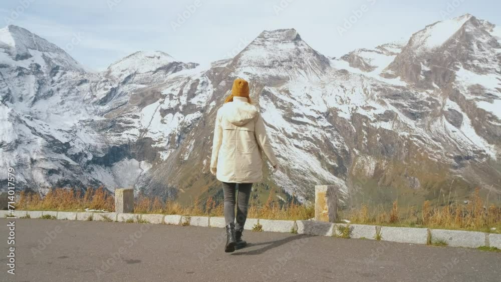 Beautiful girl traveler walks along Majestic Grossglockner Mountain Road in Austria, snow covered sharp peaks of the alpine mountains on background. Incredibly beautiful views in the Alpine mountains Beautiful girl traveler walks along Majestic Grossglockner Mountain Road in Austria, snow covered sharp peaks of the alpine mountains on background. Incredibly beautiful views in the Alpine mountains