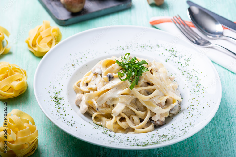 Studio photo of a beautifully plated and styled fettucine with chicken and cream in a white plate on a green wooden table Studio photo of a beautifully plated and styled fettucine with chicken and cream in a white plate on a green wooden table