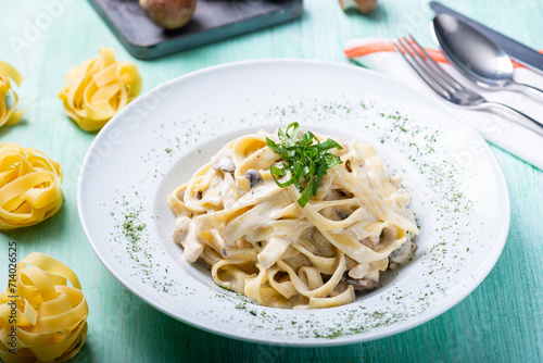 Studio photo of a beautifully plated and styled fettucine with chicken and cream in a white plate on a green wooden table