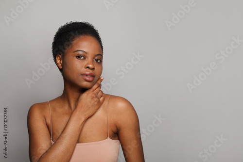 Positive healthy african american woman with clear fresh dark skin posing on gray background, fashion beauty portrait