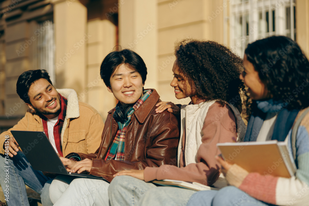 Obraz premium Smiling students with laptop is studying outdoors sitting near university. Education concept