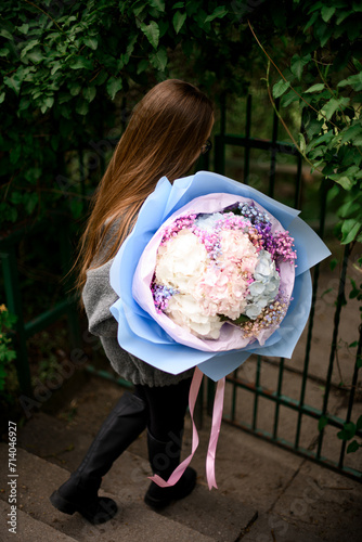 Pretty woman is walking down the steps and holding a huge bouquet of hydrangeas with hypophylla photo