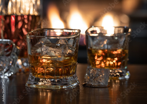 Glasses of whiskey and decanter with burning fireplace in background