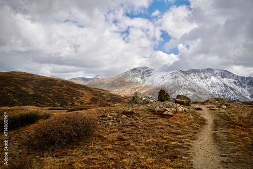 A hiking trail and snowcapped mountain with a cloudy sky on a sunny autumn day in Colorado