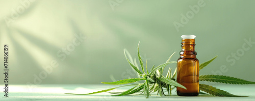 Small brown bottle with green cannabis plant on light backdrop with shadows. Alternative medicine, essential oil, herbal therapy, natural extracts, and wellness concept. Banner with copy space. photo