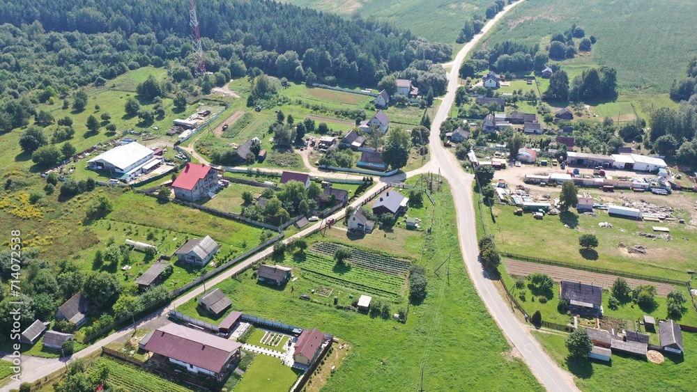 A crossroads, a fork in a village that stands in a green valley surrounded by forest. Aerial view of a European village with one-story houses, cottages. Land plots, personal plots of farmers. A crossroads, a fork in a village that stands in a green valley surrounded by forest. Aerial view of a European village with one-story houses, cottages. Land plots, personal plots of farmers.