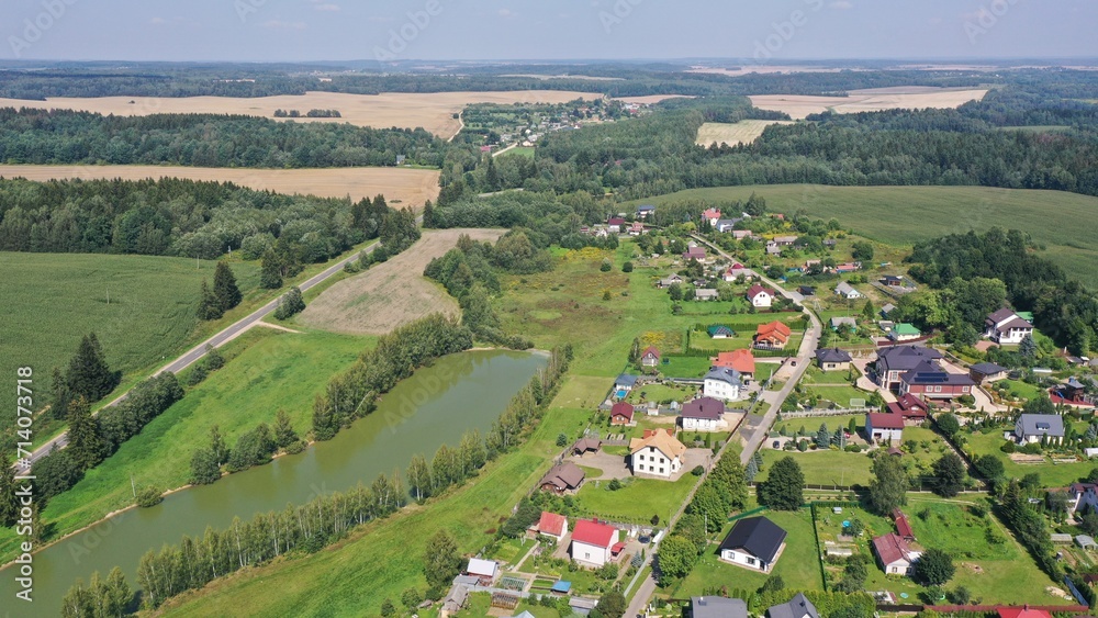 Aerial view of a rural settlement, a village in a valley, in a lowland with a pond in the middle of a picturesque forest and mountains in Europe. Lake, pond in the village in summer.