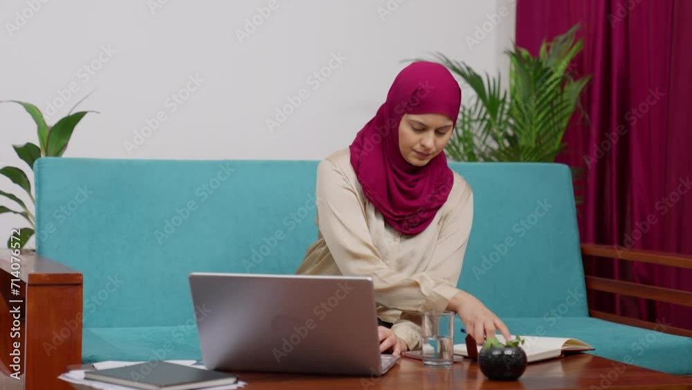 Muslim Business Woman in Hijab Scarf Sitting on Couch Working on Laptop and Taking Notes Muslim Business Woman in Hijab Scarf Sitting on Couch Working on Laptop and Taking Notes