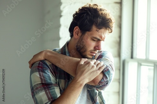 man wearing a shirt touching his shoulder in pain photo