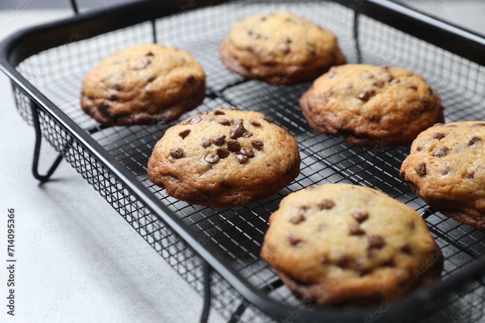 Cooling rack with delicious chocolate chip cookies on light grey table, closeup