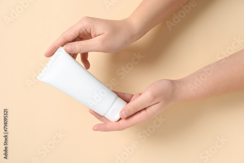 Woman with tube of hand cream on beige background, closeup