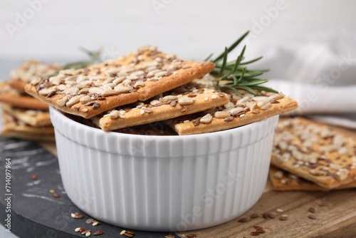 Cereal crackers with flax, sunflower, sesame seeds and rosemary in bowl on board, closeup