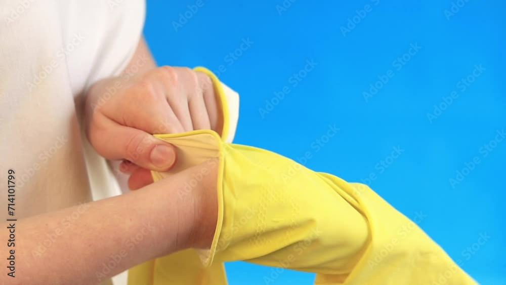 Female hands in latex gloves for cleaning the room and washing dishes. Professional cleaning. Household gloves, yellow, size M. Put gloves on your hands, blue background Female hands in latex gloves for cleaning the room and washing dishes. Professional cleaning. Household gloves, yellow, size M. Put gloves on your hands, blue background