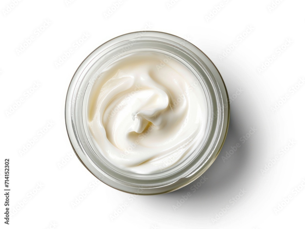 A jar of white cream is shown from above, with the lid off and the cream swirling. The jar is made of clear glass and sits on a white surface. A jar of white cream is shown from above, with the lid off and the cream swirling. The jar is made of clear glass and sits on a white surface.