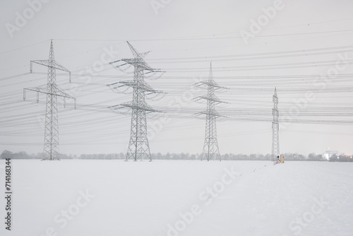 A lot of high-voltage power line in winter, electrical energy transmission tower overhead line masts, high voltage pylons as power pylons on the fields in winter with lots of snow on the fields