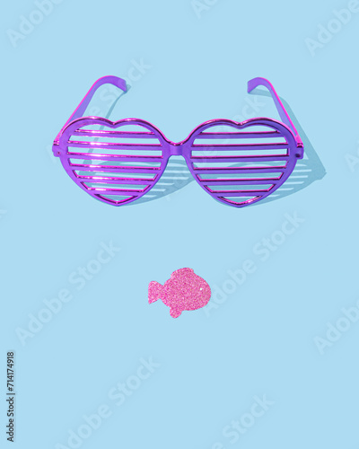 Purple eyeglasses and fish shape mouth on pastel blue background. Minimal summer party concept. Silhouette of face.