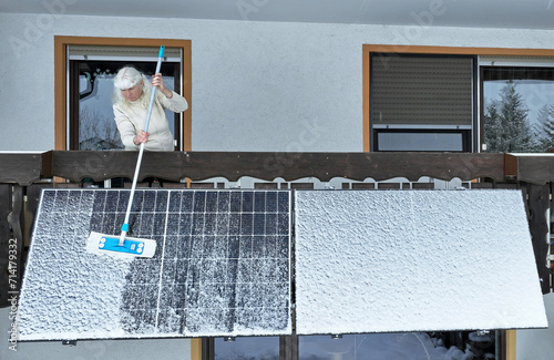 Eine Frau befreit im Winter ein Balkonkraftwerk vom Schnee
