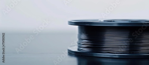 Black 3D printer filament on dark surface, white background, 1.75" diameter, ready for additive manufacturing. Close-up, spool flat.