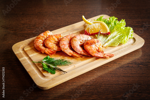 Grilled shrimp with lemon and lettuce on a wooden board.