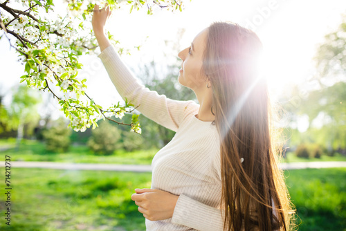 Portrait of a woman in a beautiful dress posing next to a flowering tree in a autumn park at sunset. The concept of femininity, happiness and love.