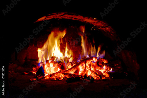 Flames dance above wood logs, casting a warm glow in the dark space.
