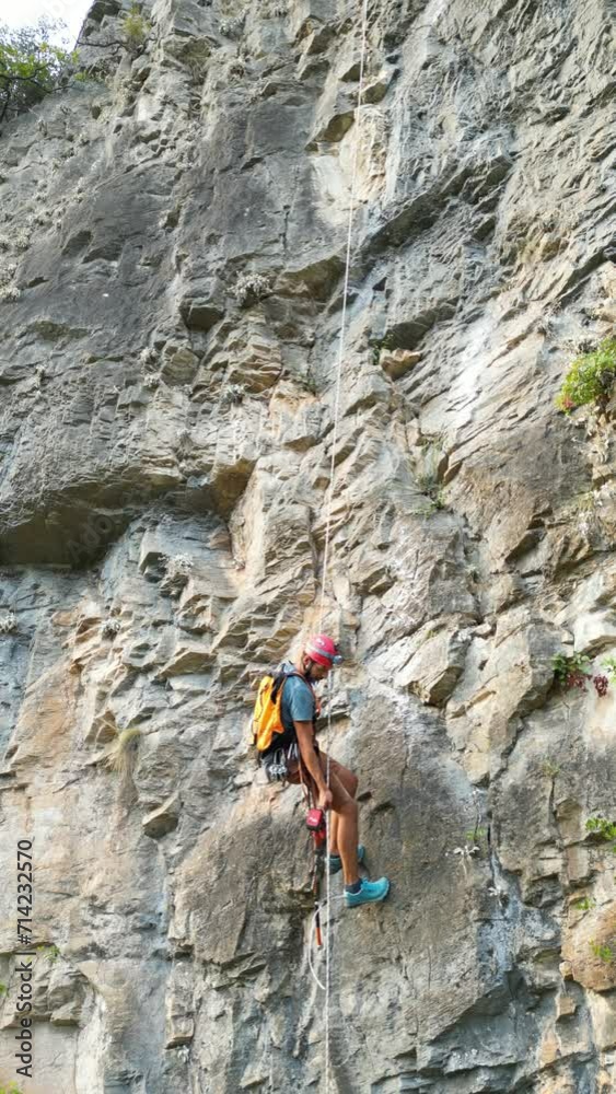 Climber going down with a rope after creating a new climbing route by using rock drills and rotary hammers on the climbing rope. Climber wears a red helmet. Climber going down with a rope after creating a new climbing route by using rock drills and rotary hammers on the climbing rope. Climber wears a red helmet.