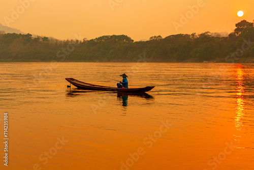 pêcheur avec dans une barque avec son chapeau au coucher de soleil