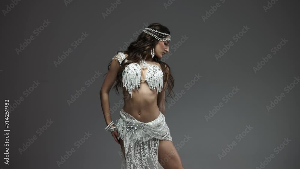 Belly and body of a woman dancing oriental dance in the studio, making beautiful body movements, she is dressed in a chic white suit on a dark background of the studio. The concept of beautiful images
