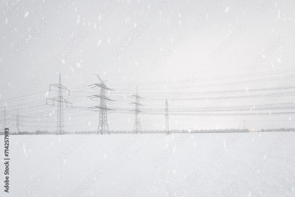 A lot of high-voltage power line in winter with lots of snow on the fields, electrical energy transmission tower overhead line masts, high voltage pylons as power pylons on the fields in winter 