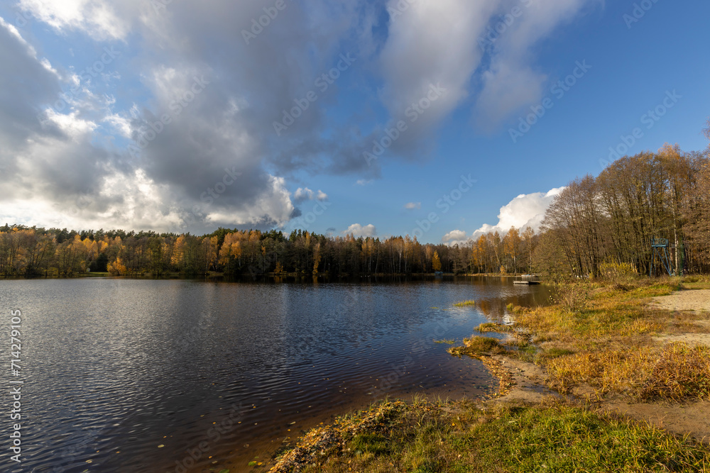 Bright autumn landscape with a river and blue sky with clouds reflected in the water