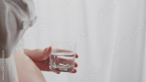 Abdominal condition. A European woman in modern clothes slowly takes medical pills near the window. Close-up of white woman drinking water from pills prescribed by doctor newborn care, prenatal photo