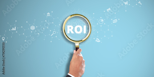 ROI. Businessman Hand Holding a Magnifying Glass with Return on Investment (ROI) Icon on Light Blue Background. Financial Analysis, Profitability, Strategic Planning. photo