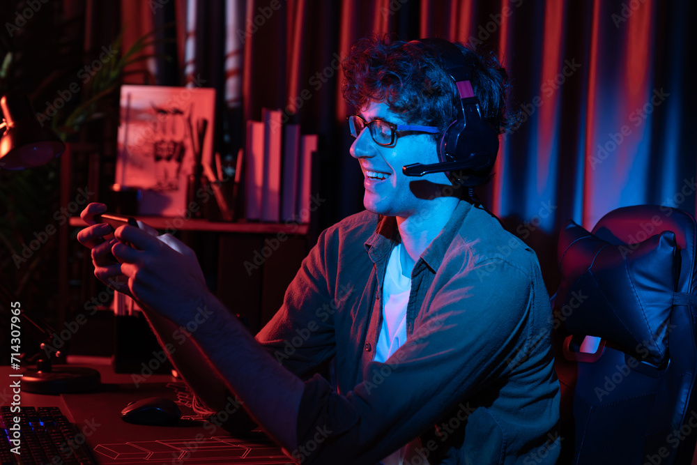 Smiling young gaming streamer team playing with Esport online on smartphone fighting wearing headphones at neon light room. Practising strategy plan to win competitors for next harder level. Gusher.