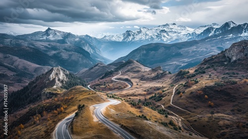  a winding road in the mountains with a view of a mountain range in the distance with a snow - capped mountain range in the distance, and a cloudy sky filled with clouds.