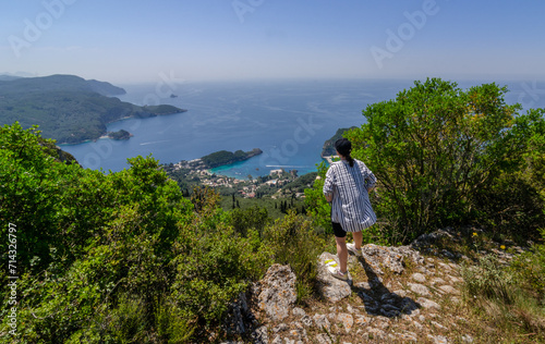 Traveler hiker girl enjoying landscape of Palaiokastritsa in Corfu, Greece from a mountain top during hot summer day
