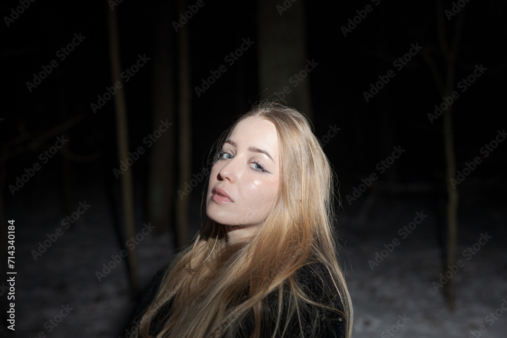 Fototapeta premium Young blond Woman with black dress in the wood at an snowstorm in deep winter at berlin forrest
