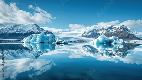  a group of icebergs floating on top of a lake next to a snow covered mountain under a blue sky with clouds and a few puffy white clouds.