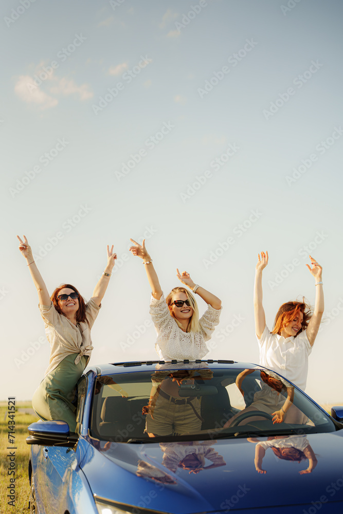 Foto de Three friends pop out of a car sunroof, arms raised in joy ...