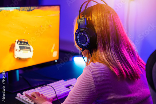 Young player woman wearing gaming headphones intend to do playing live stream games online at home, Happy Gamer endeavor plays online video games tournament with computer with neon lights, Back view