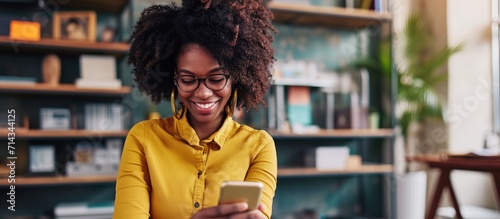 Joyful black woman, using phone for networking or social media at office. African employee enjoying online browsing or chat on smartphone at work.