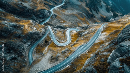  an aerial view of a winding road in a mountainous area with snow on the ground and yellow patches of grass on the side of the road and yellow patches of grass on the side of the road. © Anna