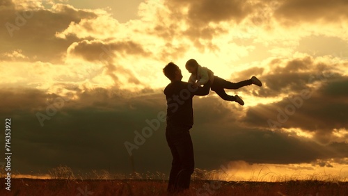 Fototapeta Naklejka Na Ścianę i Meble -  Concept, family safety trust, Dad plays with his daughter, throws child into sky with his hands, happy kid. Silhouette, Father of daughters playing together in park against backdrop of sun and clouds