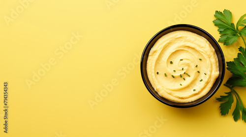 Bowl of hummus with greens and olive oil on yellow background, top view, copy space